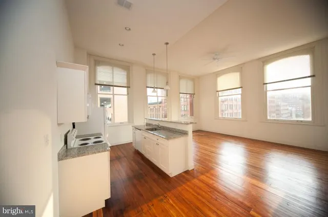 a kitchen with granite countertop a stove a sink and white cabinets with wooden floor next to windows