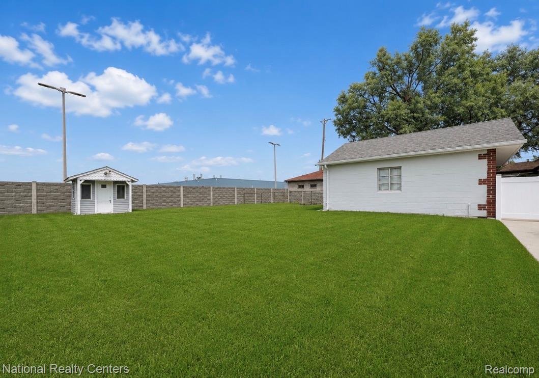 7285 Helen Street Center Line, MI 48015 - Photo 29 of 32 Expansive grass lawn featuring a detached shed, concrete perimeter fencing, and a white house with a brick accent