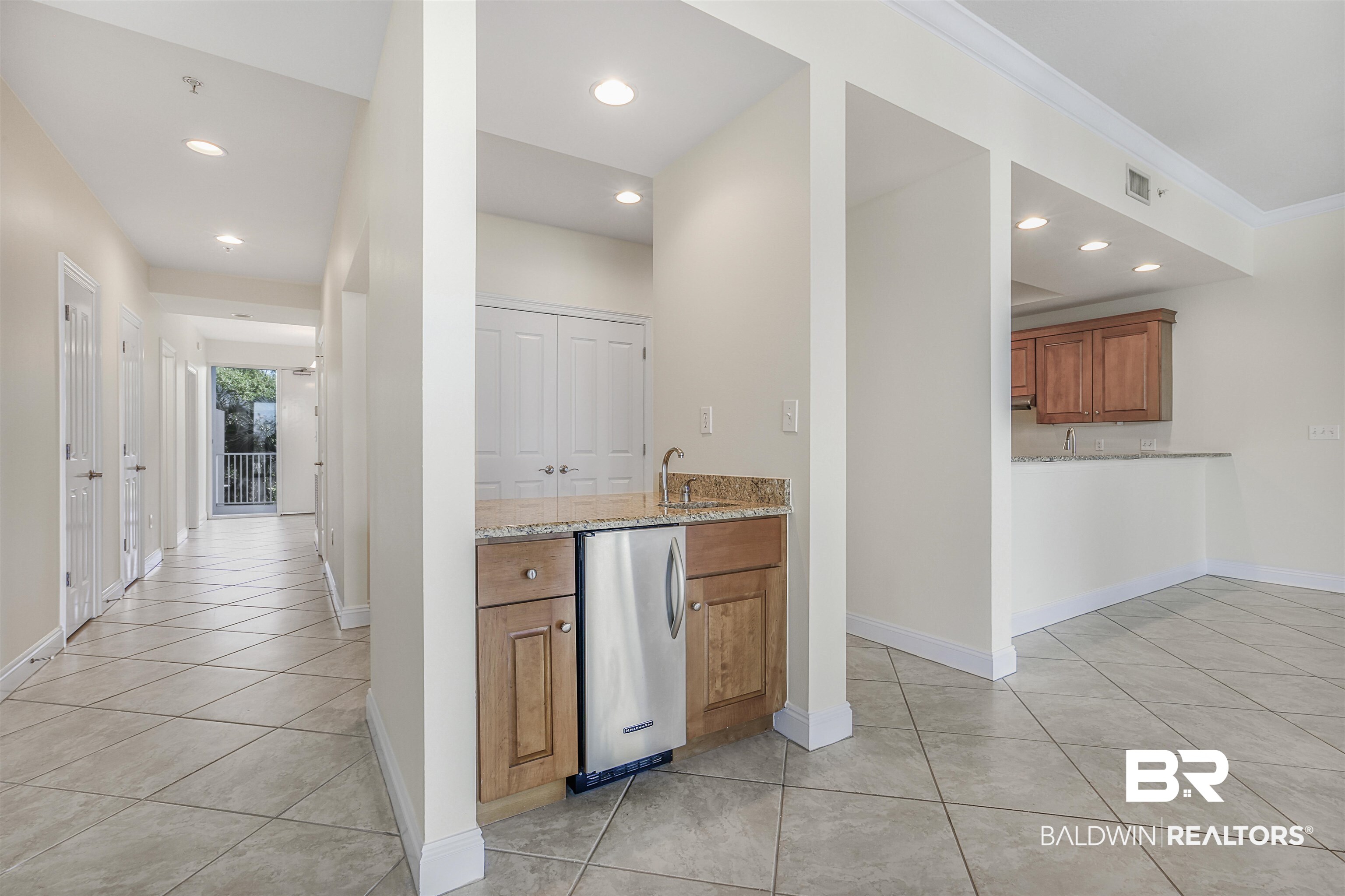 28250 Canal Road, Unit 106 Orange Beach, AL 36561 - Photo 3 of 50 Kitchen with brown cabinetry, light stone countertops, recessed lighting, light tile patterned floors, and stainless steel refrigerator