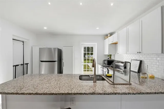 a kitchen with kitchen island granite countertop a sink a stove a refrigerator cabinets and living room view