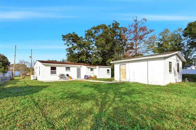 a house that is sitting in the grass with large trees and plants