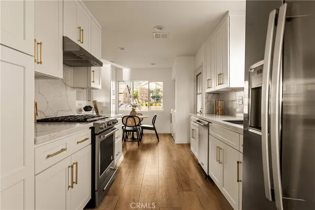a kitchen with stainless steel appliances a stove a sink dishwasher a refrigerator white cabinets and wooden floor