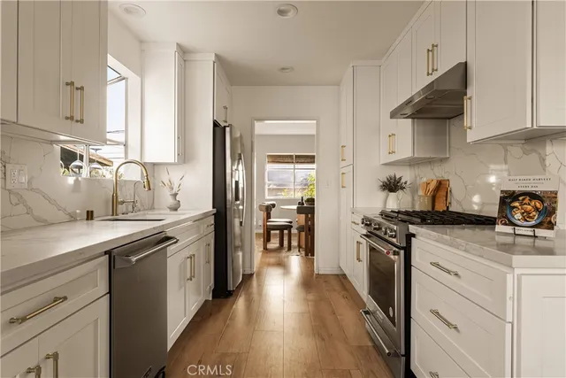 a kitchen with stainless steel appliances a sink dishwasher stove refrigerator and cabinets with wooden floor