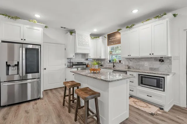 a kitchen with stainless steel appliances a stove a sink a refrigerator and white cabinets with wooden floor