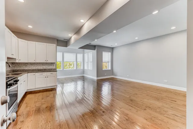 a view of an empty room and kitchen with wooden floor