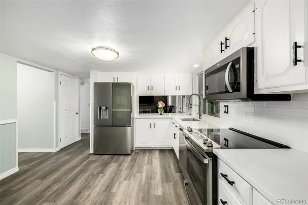 a kitchen with stainless steel appliances a stove top oven a sink a refrigerator white cabinets and wooden floor