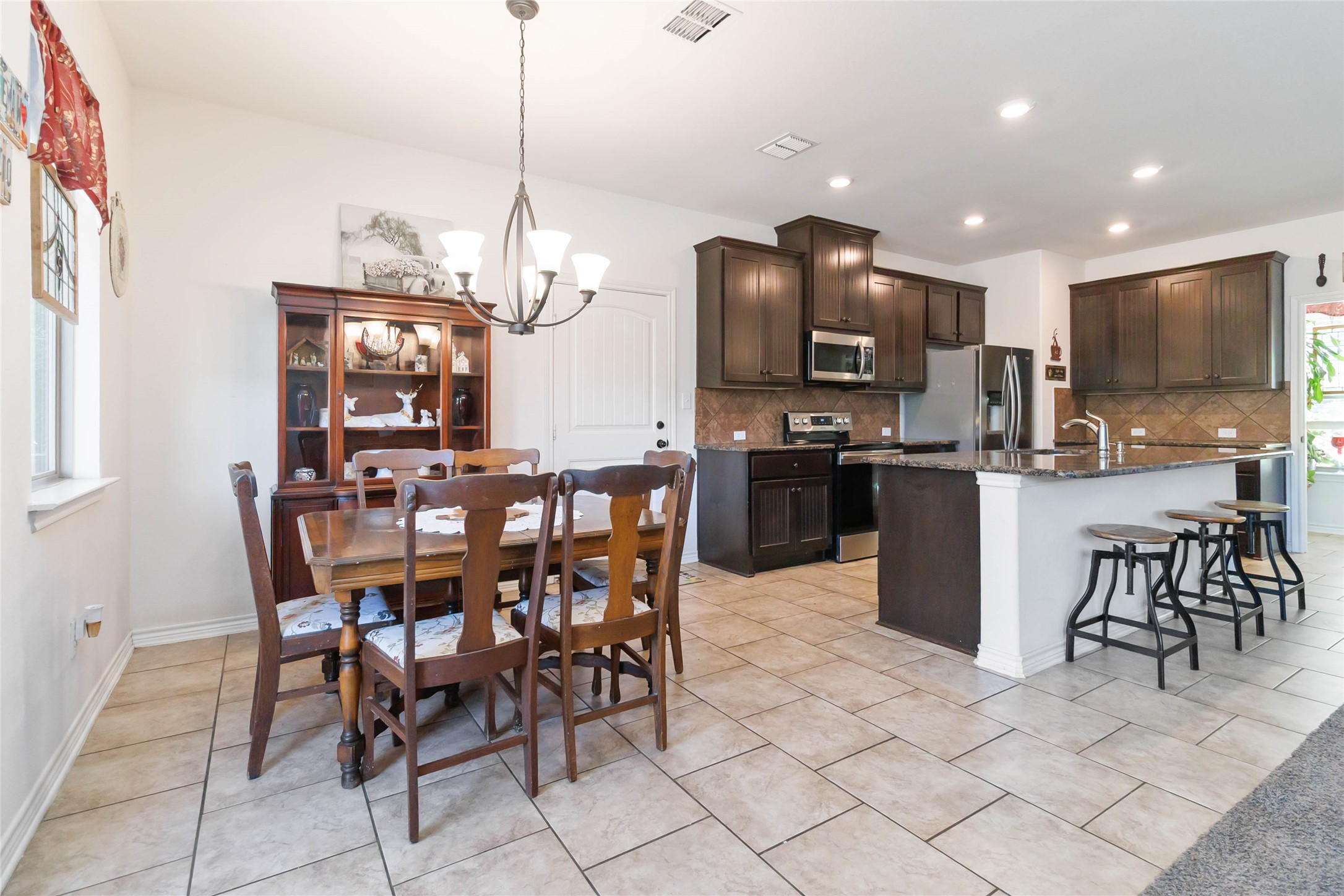 1193 Persimmon Pass Fischer, TX 78623 - Photo 14 of 27 Kitchen with dark brown cabinets, a kitchen bar, appliances with stainless steel finishes, a chandelier, and light tile floors
