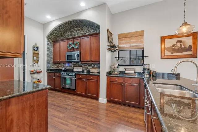 a kitchen with stainless steel appliances granite countertop a stove a sink dishwasher and a microwave oven with large wooden cabinets