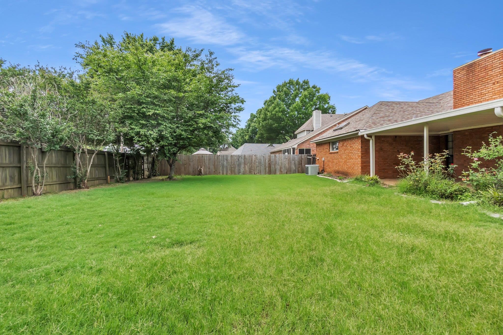 6613 Stephan Ridge Drive Bartlett, TN 38135 - Photo 23 of 24 Expansive backyard featuring a lush lawn, mature trees, wood privacy fencing, and a covered patio area
