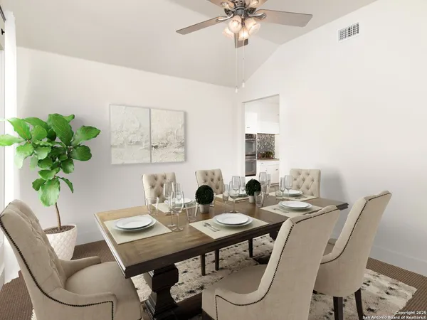 an empty room with a chandelier fan and kitchen view