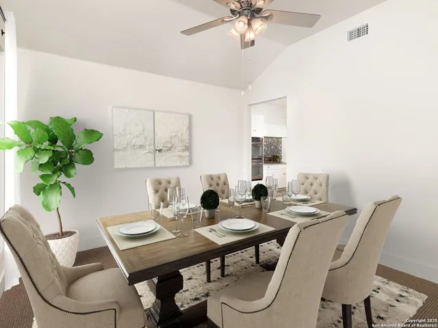 an empty room with a chandelier fan and kitchen view