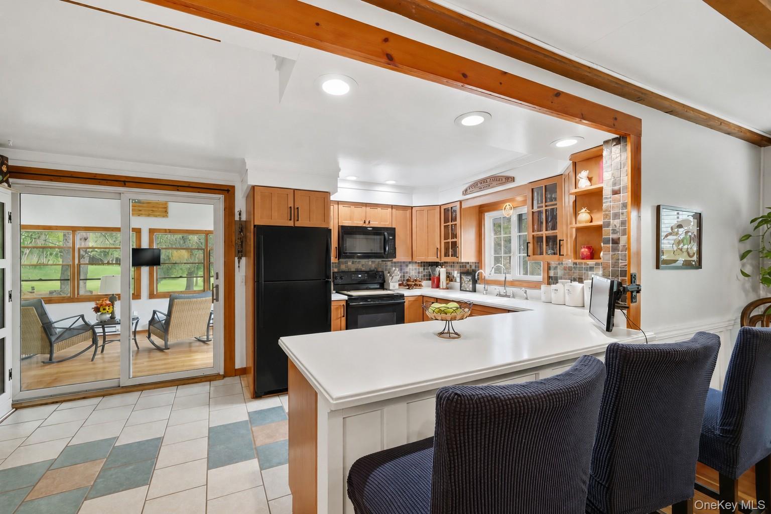 115 Cold Spring Road Liberty, NY 12754 - Photo 6 of 35 A spacious, sunlit kitchen featuring rustic warmth meets modern design, with wood cabinetry, sleek white countertops, and a charming sunroom just beyond. Bright, cozy, and beautifully arranged, the space includes a welcoming island, natural wood trim, and a harmonious blend of functional appliances, decorative accents, and endless greenery visible through large windows. Reverse osmosis faucets in kitchen.