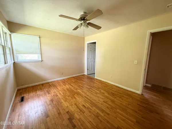 an empty room with wooden floor fan and windows
