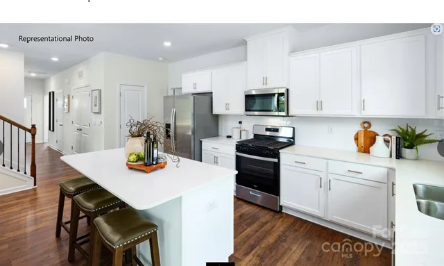 a kitchen with stainless steel appliances kitchen island granite countertop a refrigerator a stove a sink dishwasher and white cabinets with wooden floor