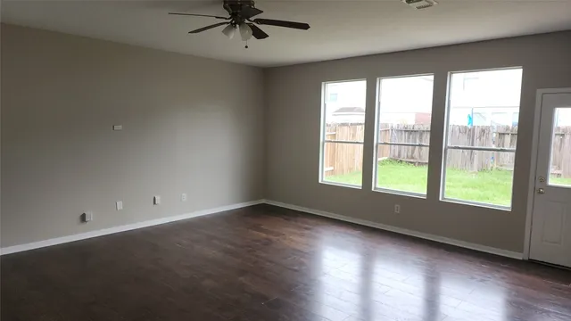 an empty room with wooden floor fan and windows