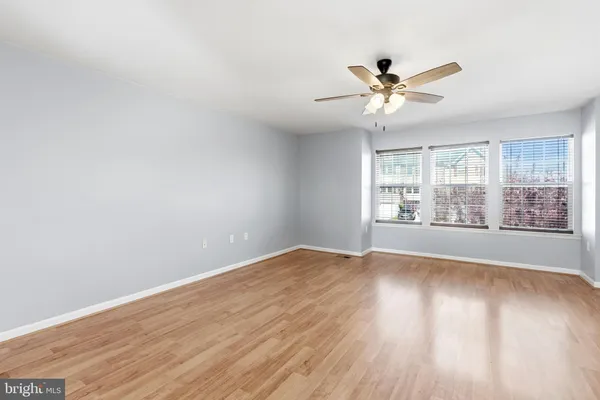 an empty room with wooden floor fan and windows