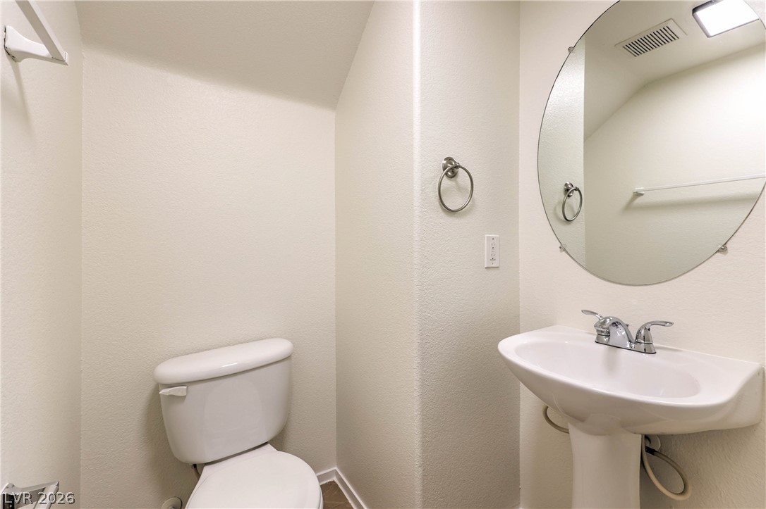 10939 Paradise Road Henderson, NV 89052 - Photo 17 of 36 A compact powder room with a sleek pedestal sink and round mirror provides essential convenience.