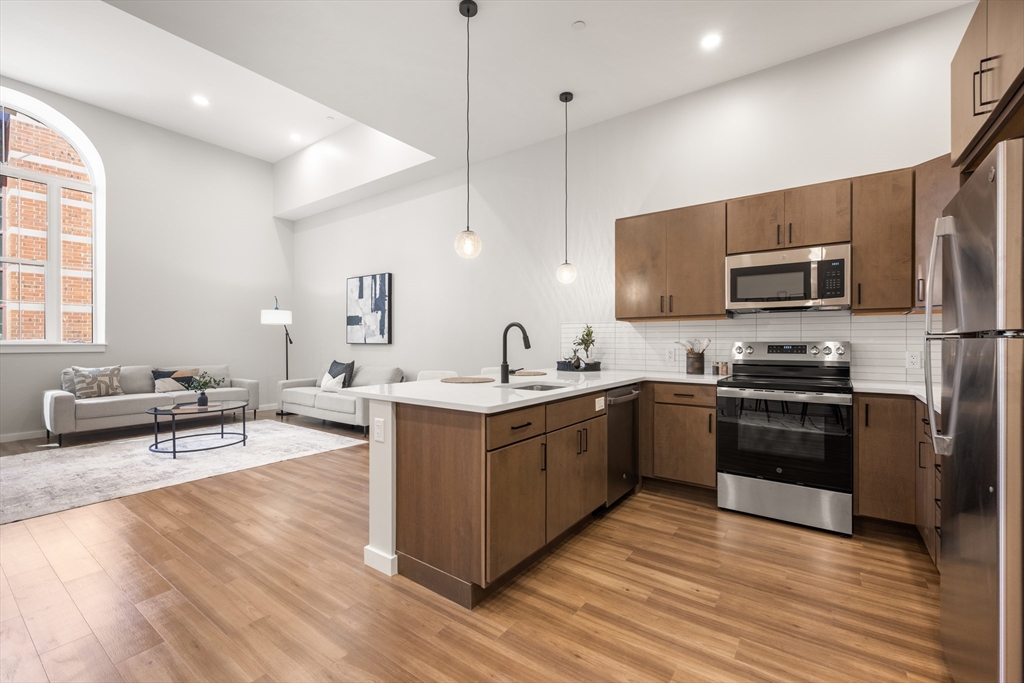22 Elm Street, Unit 302 Worcester, MA 01608 - Photo 5 of 18 a large kitchen with stainless steel appliances granite countertop a stove a sink dishwasher a microwave oven and a dining table with wooden floor