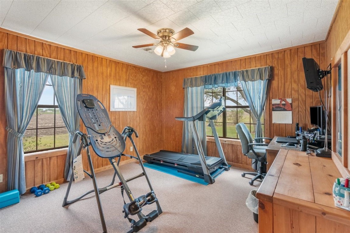 13339 Bj Dusek Road Wallis, TX 77485 - Photo 12 of 39 This room features wood-paneled walls and is set up as a home gym and office. It includes bright natural light from two large windows with blue curtains, offering a view of the outdoors.