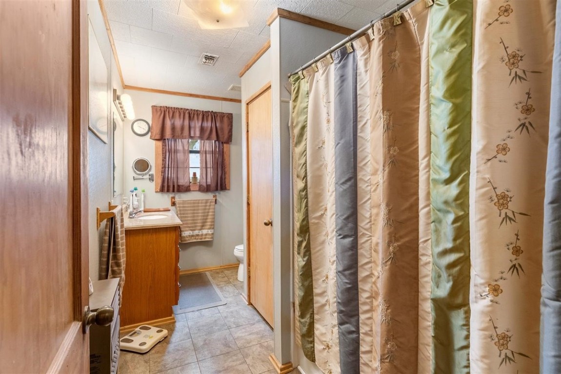 13339 Bj Dusek Road Wallis, TX 77485 - Photo 13 of 39 This bathroom features a cozy design with a shower-tub combo, patterned curtain, single vanity with a mirror, and a window with a decorative curtain for natural light. The space is functional with tiled flooring and warm wood accents.