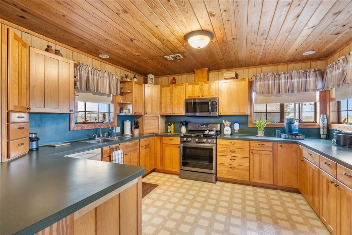 13339 Bj Dusek Road Wallis, TX 77485 - Photo 15 of 39 This kitchen features warm wooden cabinetry and a wood-paneled ceiling, creating a cozy, rustic feel. It includes modern appliances, ample counter space, and large windows for natural light. The layout is open and inviting, perfect for cooking and entertaining.
