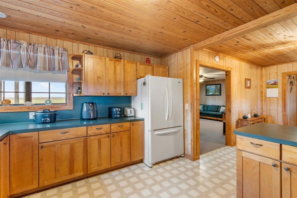 13339 Bj Dusek Road Wallis, TX 77485 - Photo 19 of 39 This cozy kitchen features warm wood paneling and cabinetry, a white refrigerator, and teal countertops. A window offers natural light and views outside, while an adjoining room provides additional living space.