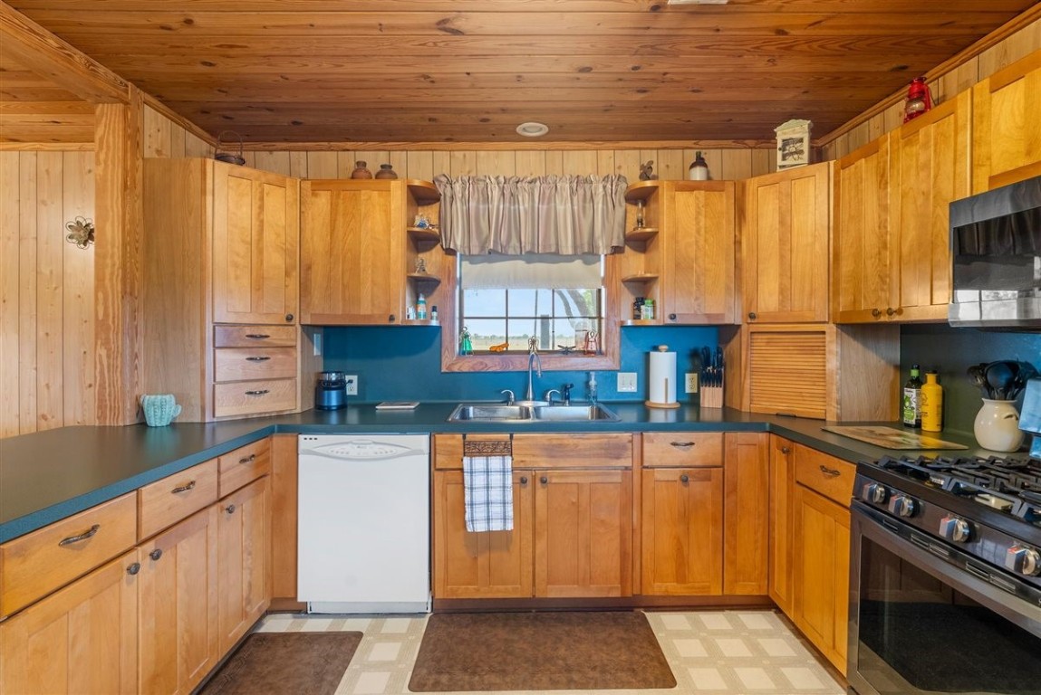 13339 Bj Dusek Road Wallis, TX 77485 - Photo 20 of 39 This cozy kitchen features warm wooden cabinetry and ceiling, complemented by a teal backsplash. It includes modern appliances, a double sink, and ample counter space, creating a welcoming and functional cooking area.
