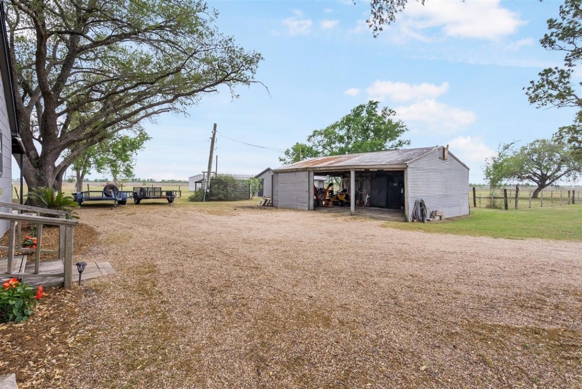 13339 Bj Dusek Road Wallis, TX 77485 - Photo 22 of 39 This photo features a rustic property with a large gravel driveway, a metal storage shed, and mature trees, offering ample outdoor space and a rural setting.