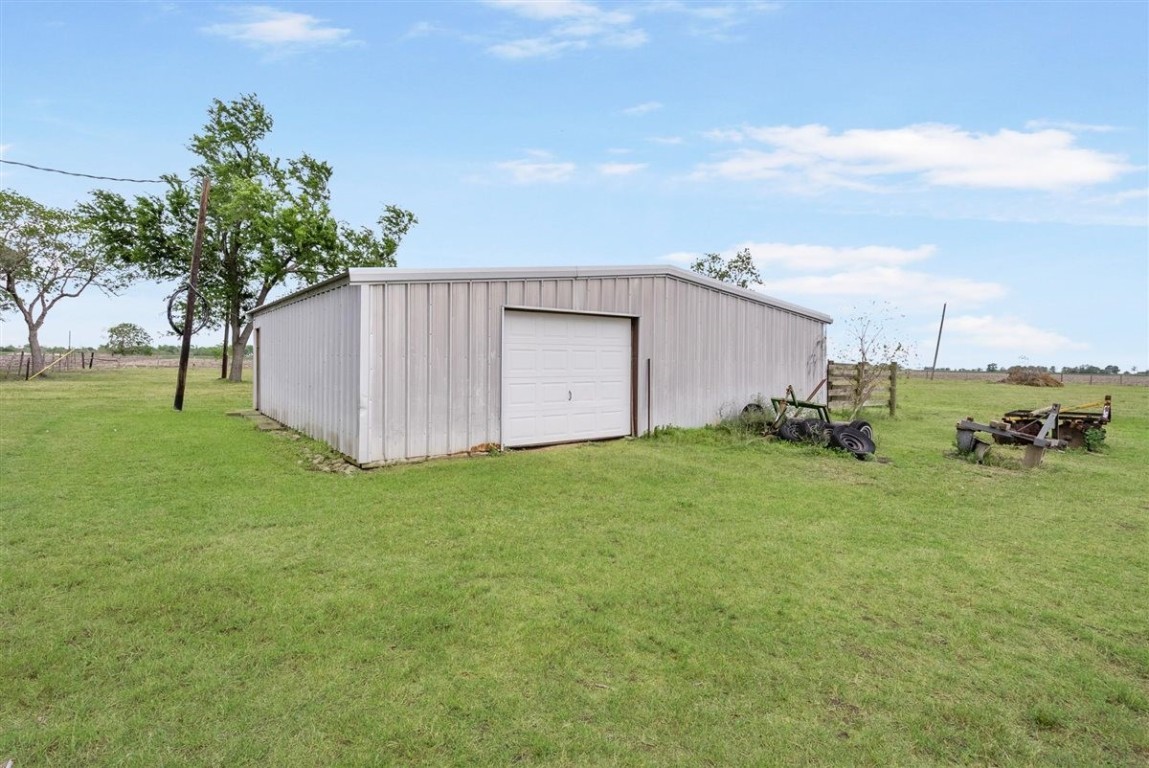 13339 Bj Dusek Road Wallis, TX 77485 - Photo 24 of 39 This photo shows a spacious metal storage building with a roll-up garage door, situated on a large grassy lot. Ideal for additional storage or workshop needs, it offers a rural setting with open land and a few scattered trees.