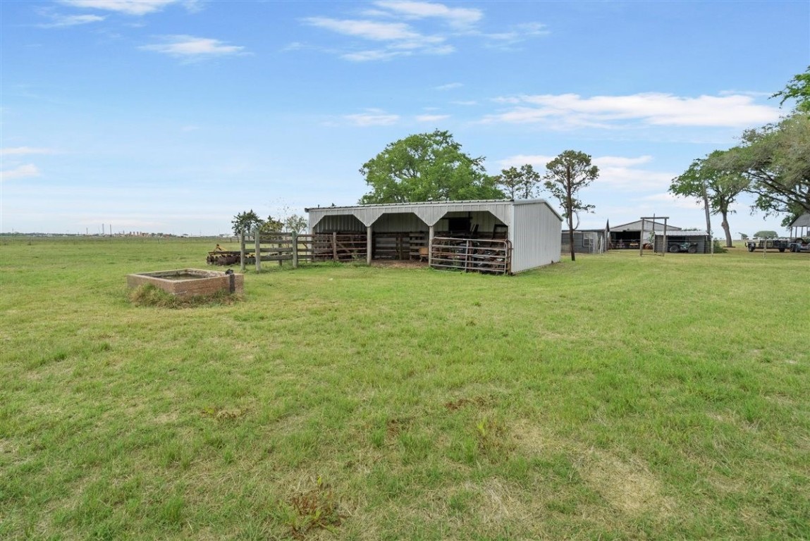 13339 Bj Dusek Road Wallis, TX 77485 - Photo 27 of 39 This photo shows a spacious, open field with a metal barn structure, ideal for livestock or storage. The area is surrounded by a few trees and has a clear, expansive view, perfect for agricultural use or rural living.