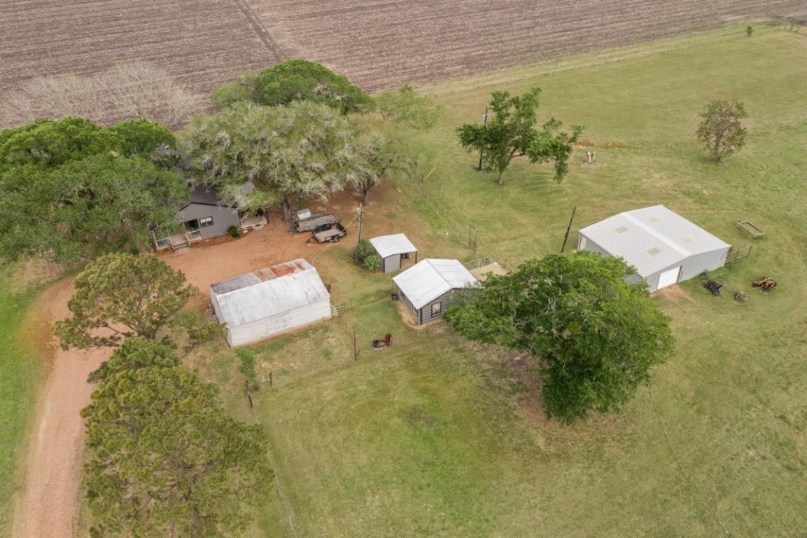 13339 Bj Dusek Road Wallis, TX 77485 - Photo 28 of 39 This aerial view showcases a rural property with multiple structures, including a main house surrounded by trees, additional outbuildings, and a large metal barn. The property is set in a spacious, open area with adjacent fields, providing ample outdoor space and privacy.