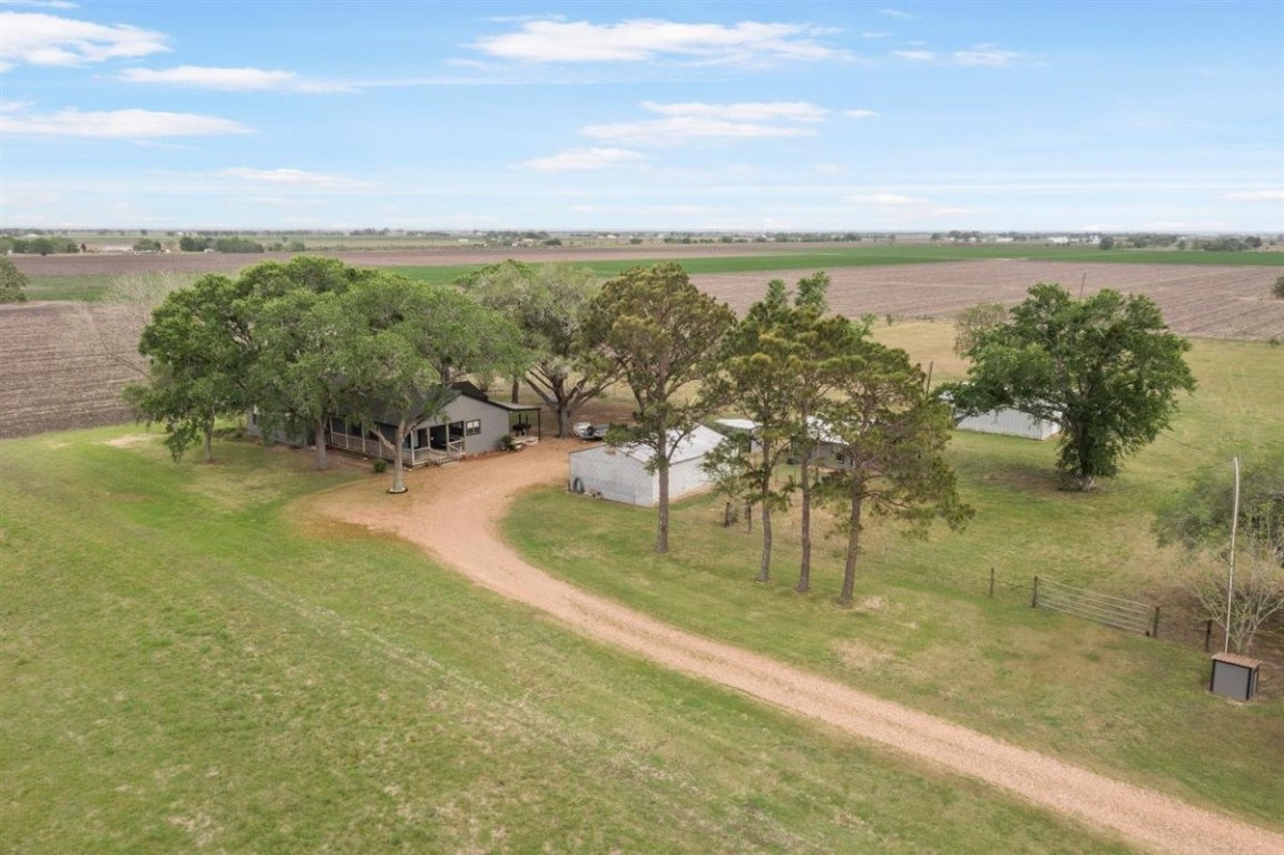 13339 Bj Dusek Road Wallis, TX 77485 - Photo 29 of 39 This photo shows a rural property with a house and outbuildings surrounded by open fields. A tree-lined driveway leads to the home, providing a peaceful, secluded atmosphere with expansive views of farmland.