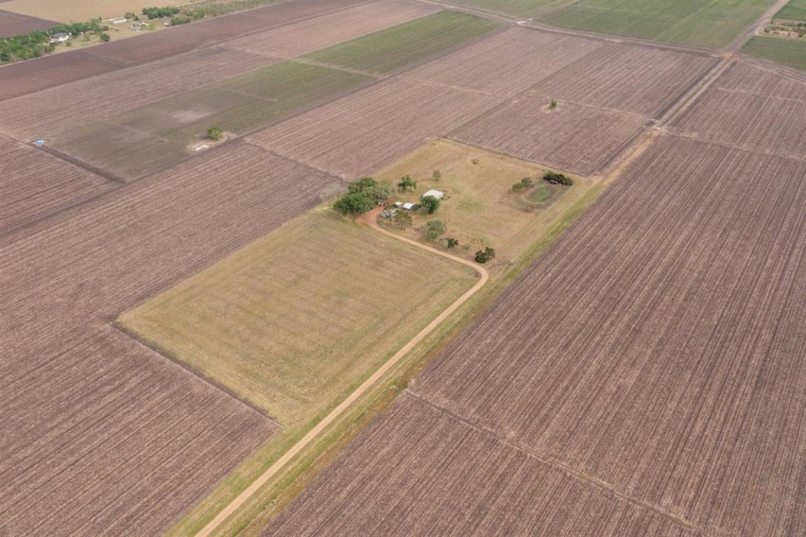 13339 Bj Dusek Road Wallis, TX 77485 - Photo 33 of 39 Aerial view of a rural property surrounded by expansive farmland. The plot features a small house with trees and a dirt access road, offering a secluded and spacious setting. Ideal for those seeking privacy and agricultural opportunities.