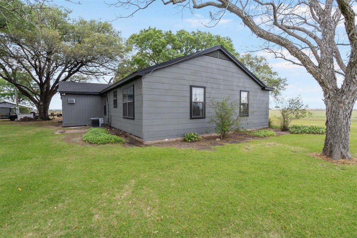 13339 Bj Dusek Road Wallis, TX 77485 - Photo 4 of 39 This photo shows a cozy, single-story gray house with a simple exterior, surrounded by a well-maintained lawn. Mature trees provide shade, and the property offers a peaceful, rural setting with open field views.