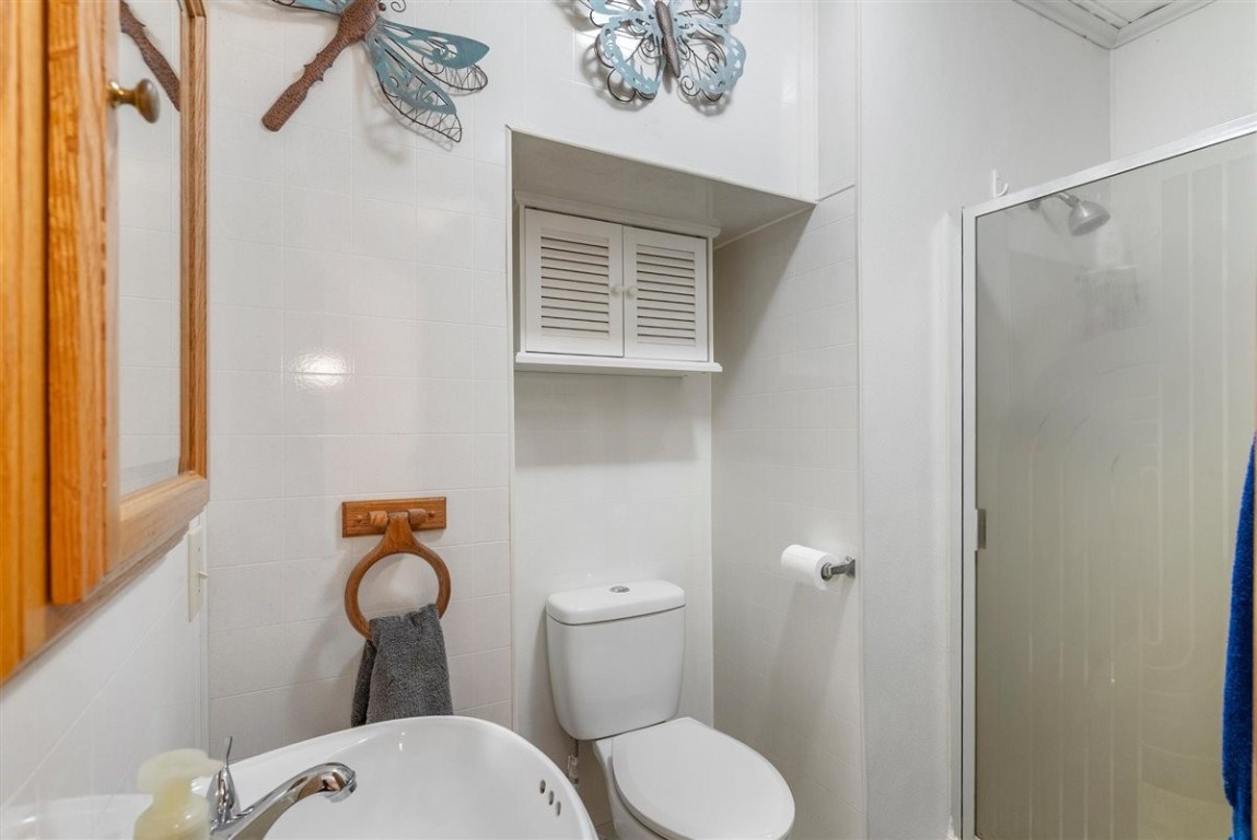 13339 Bj Dusek Road Wallis, TX 77485 - Photo 9 of 39 This bathroom features a compact design with a white color scheme. It includes a shower with frosted glass, a toilet with overhead storage, and a small sink with a wooden-framed mirror.