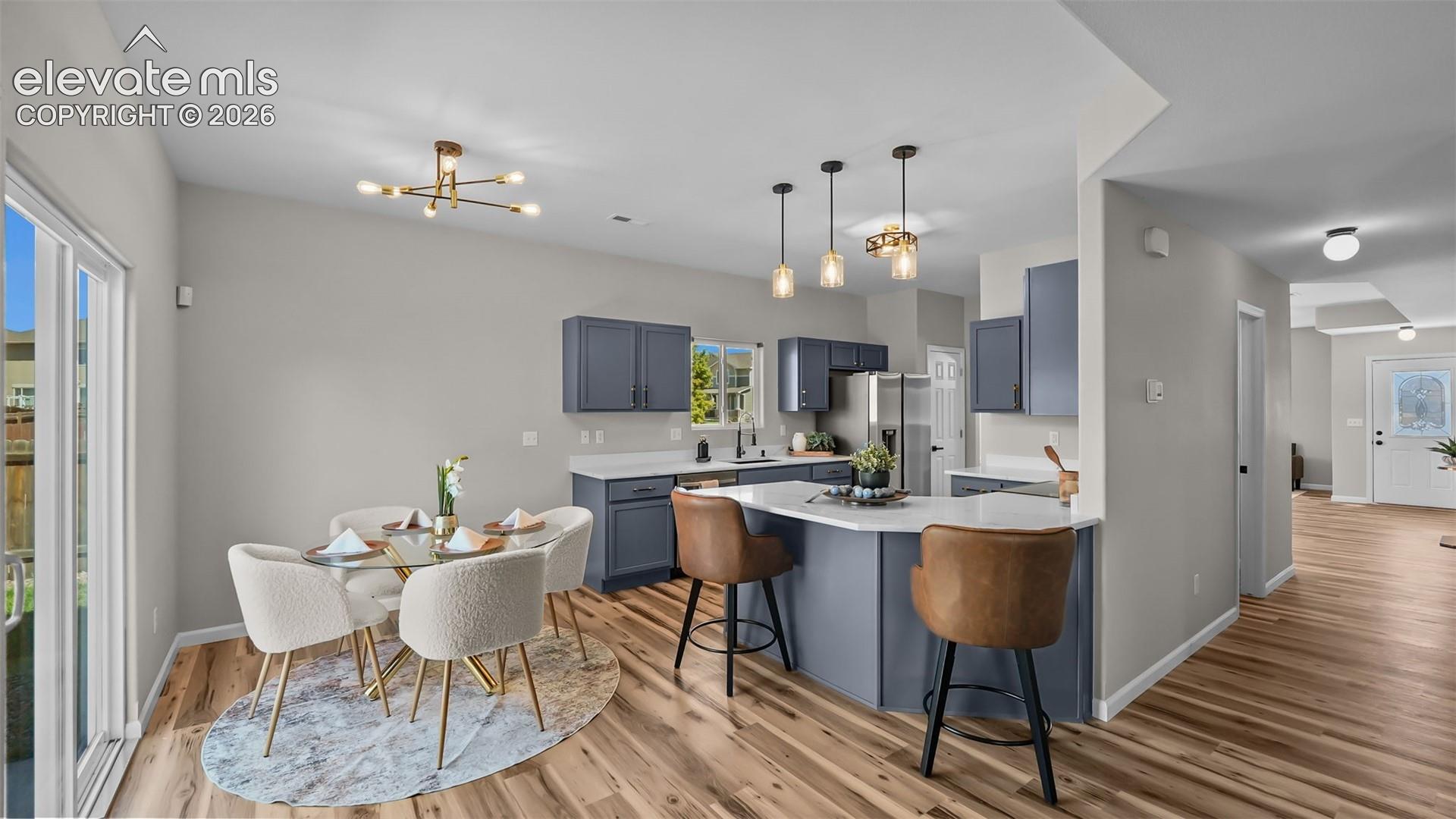 2044 Reed Grass Way Colorado Springs, CO 80915 - Photo 14 of 47 Kitchen and dining area featuring wood-finish flooring, a kitchen island with seating, pendant lighting fixtures, and sliding glass doors