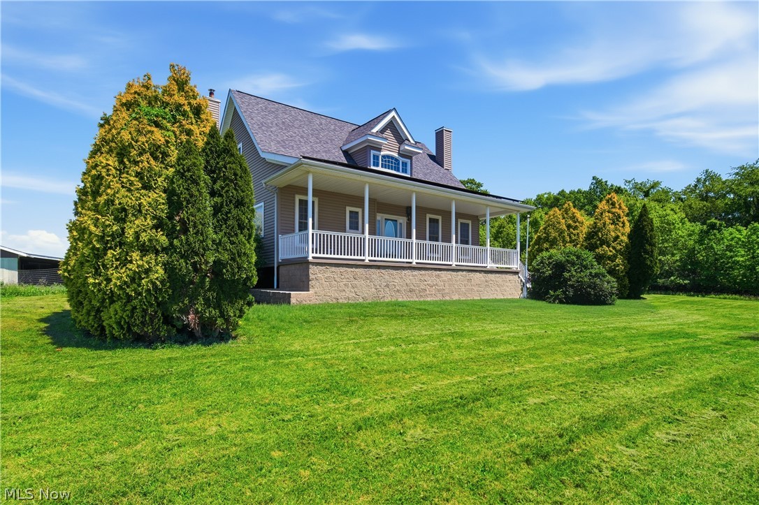 Expansive green lawn bordering a residence with a covered front porch, white railings, and mature landscaping