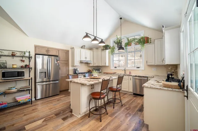 a kitchen with a refrigerator a stove a sink dishwasher and a dining table with wooden floor