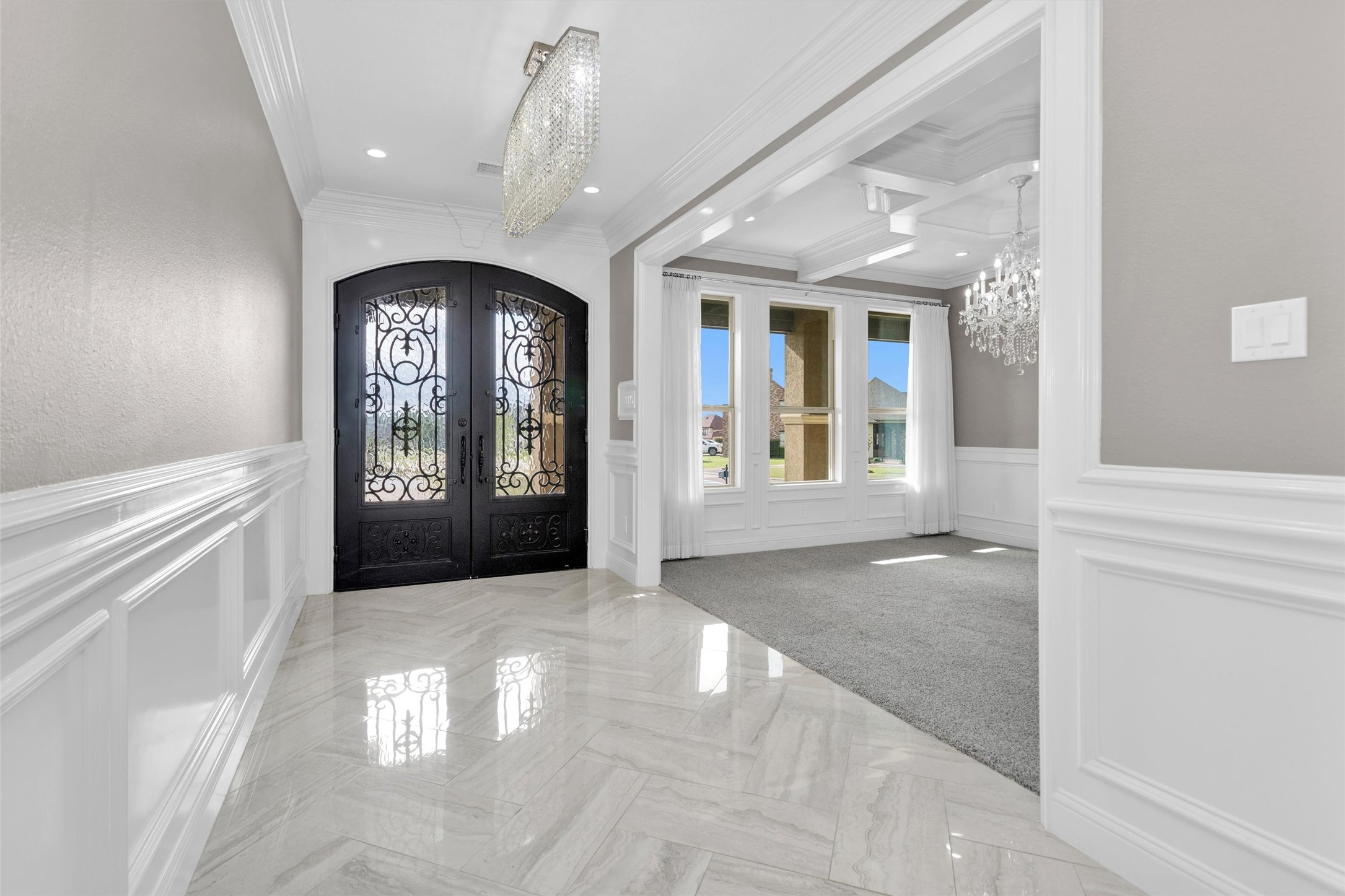 10887 Decatur Street Willis, TX 77318 - Photo 7 of 50 Striking entry with immediate impact—double iron front doors and a statement chandelier set the tone as you step into a bright, polished foyer. Glossy tile flooring runs throughout the entry, paired with crisp white wainscoting, crown molding and clean architectural lines.