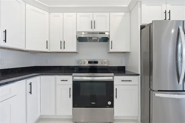 a kitchen with stainless steel appliances granite countertop a refrigerator stove and white cabinets