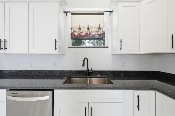 a kitchen with stainless steel appliances granite countertop white cabinets sink and a window