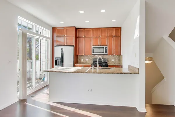 a kitchen with stainless steel appliances granite countertop a refrigerator a stove and a sink with wooden floor