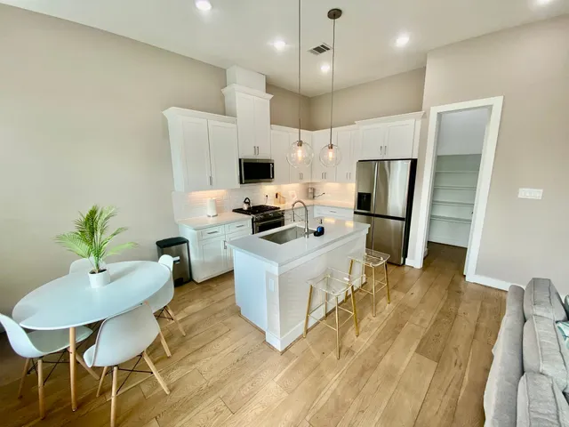 a kitchen with stainless steel appliances a stove a refrigerator and a dining table with wooden floor