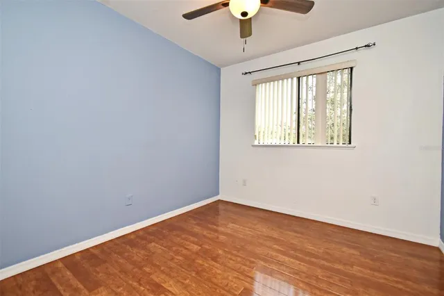 an empty room with wooden floor chandelier fan and windows