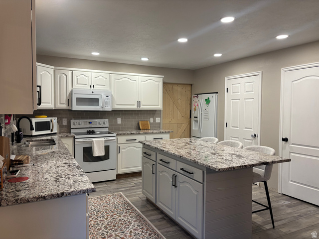 1324 West Raintree Drive, Unit 44 Price, UT 84501 - Photo 3 of 25 Modern kitchen featuring white cabinetry with black hardware, complementing a light-toned backsplash and stone-finish countertops