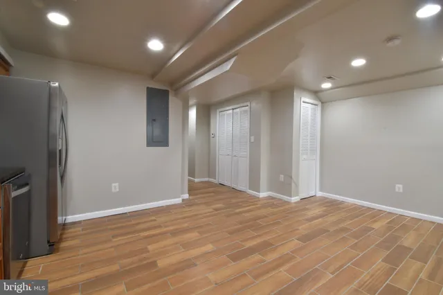 a view of an empty room with wooden floor and a kitchen