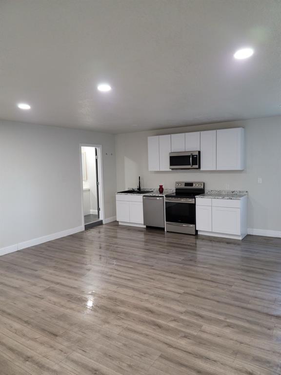 9551 Lechner Road, Unit G Fort Worth, TX 76179 - Photo 10 of 15 Open-concept living space with wood-finish flooring, recessed lighting, and a modern kitchen featuring white shaker cabinetry, stainless steel appliances, and granite countertops