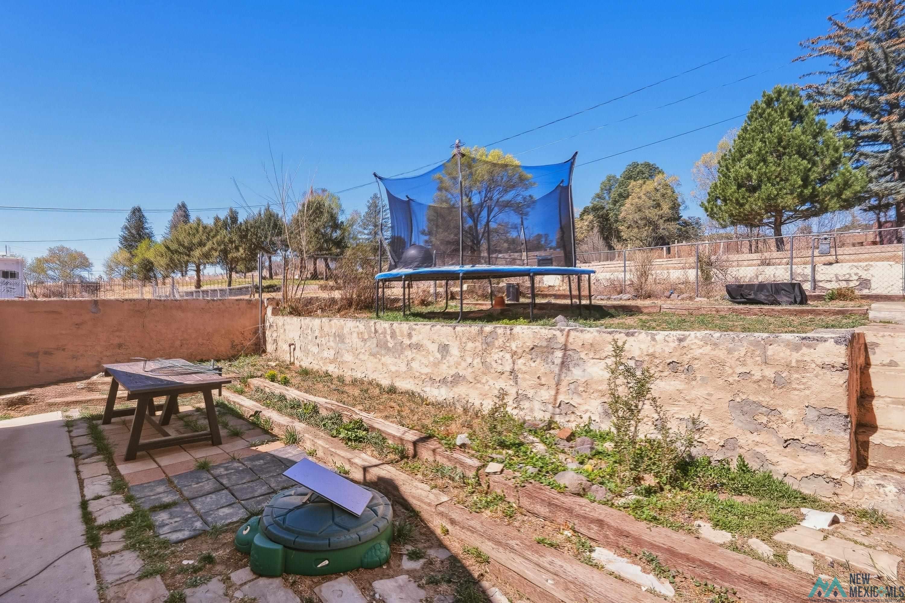 1432 South 5th Street Raton, NM 87740 - Photo 26 of 32 Fenced backyard with a trampoline, outdoor dining space, and a patio