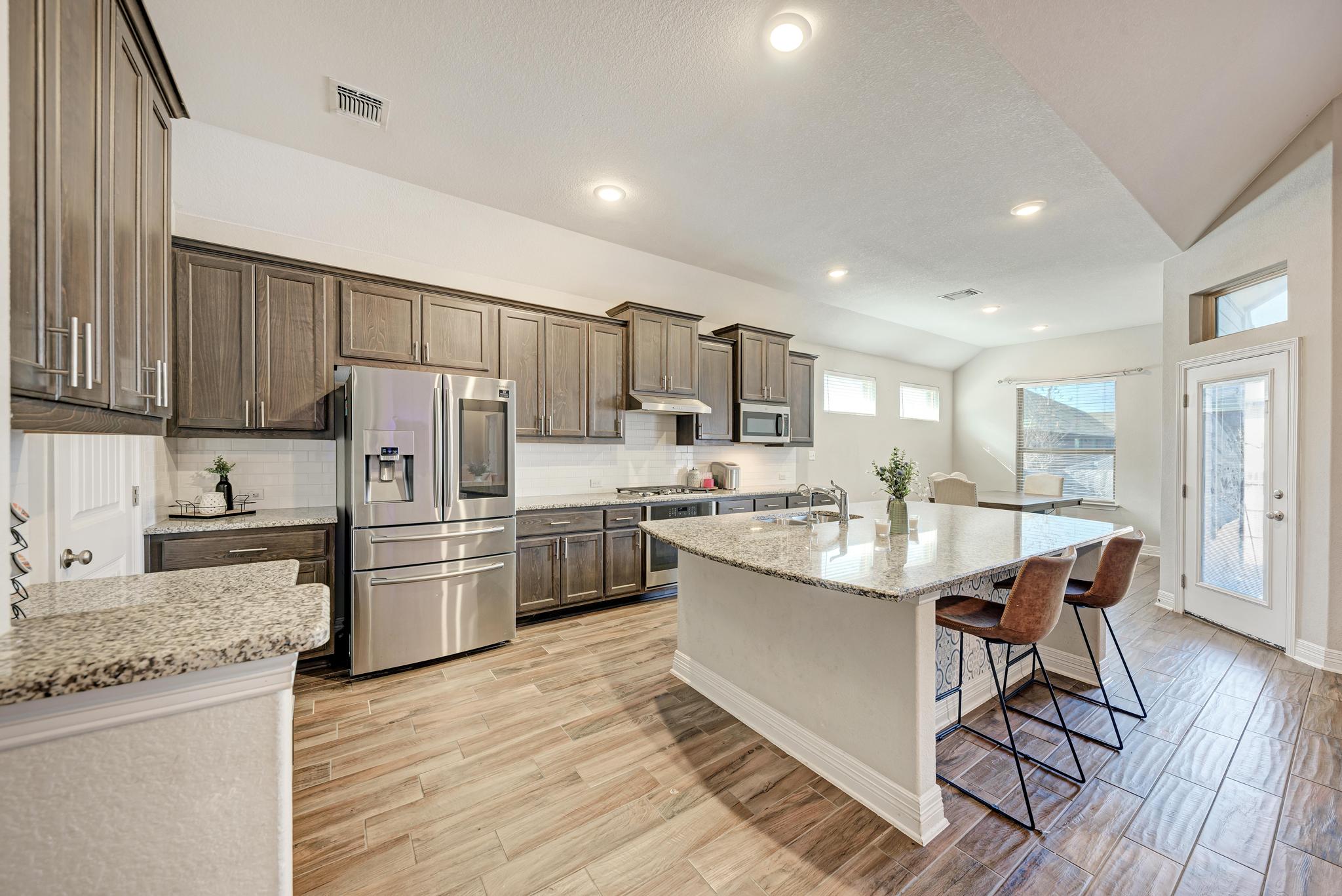 198 Rough Leaf Drive Buda, TX 78610 - Photo 11 of 38 Kitchen featuring stainless steel appliances, light stone countertops, vaulted ceiling, wood tiled floors, and backsplash