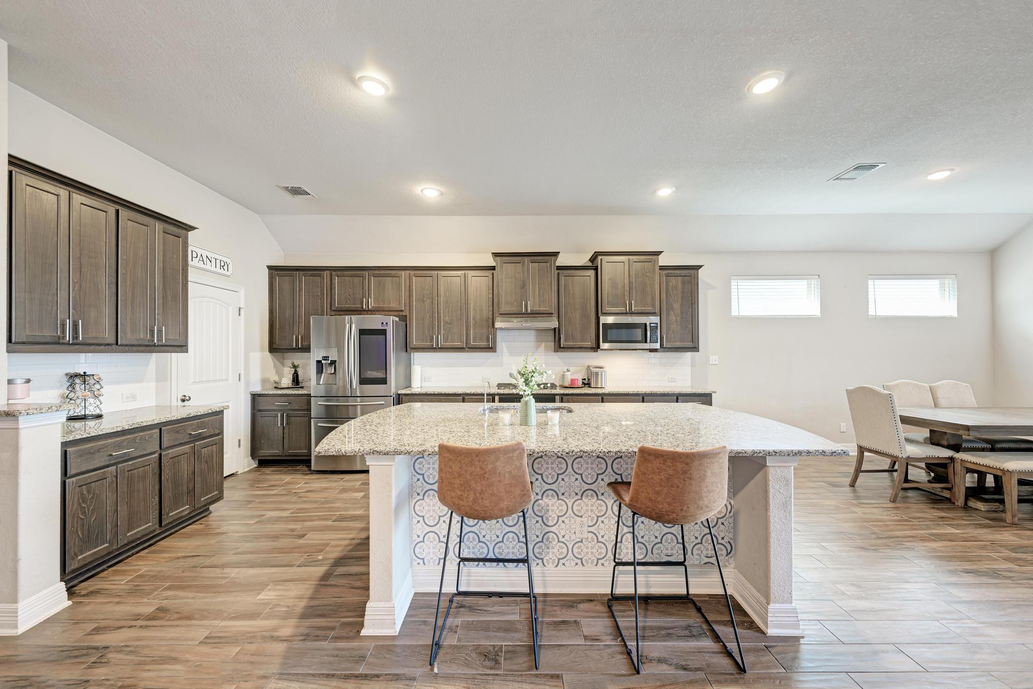 198 Rough Leaf Drive Buda, TX 78610 - Photo 12 of 38 Kitchen with dark wood finish cabinets, light stone countertops, stainless steel appliances, a breakfast bar area, and light wood-type flooring